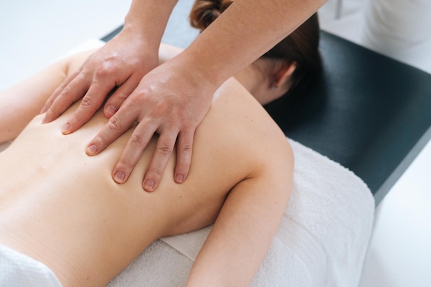 Top closeup view of male masseur massaging back and shoulders of female lying on massage table