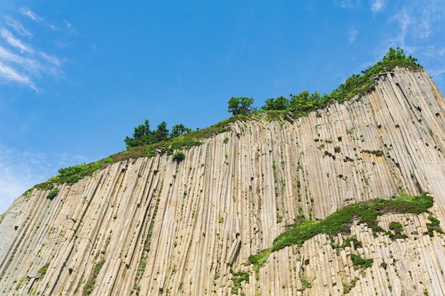 Top of columnar volcanic basalt cliff against the background of the sky with clouds