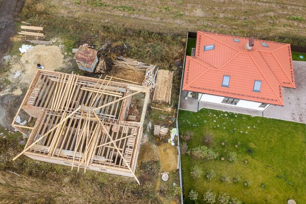 Top down aerial view of two private houses one under construction with wooden roofing frame and another finished with red tiled roof