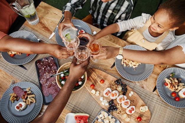 Top down portrait of big africanamerican family clinking glasses while enjoying dinner together outd...