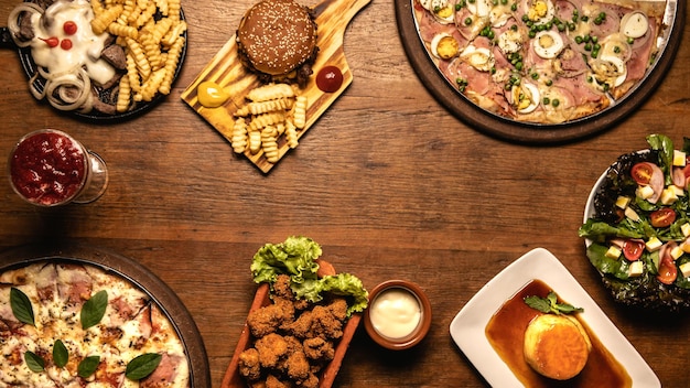 Top down of tasty meals on a wooden cutting board with pizza fried chicken hamburger and steak