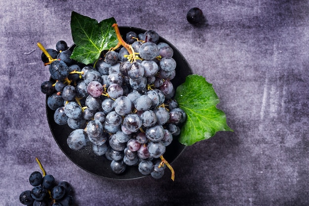 Top down view of a black grape with green leaves on the dark surface