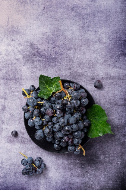 Top down view of a black grape with green leaves on the dark surface