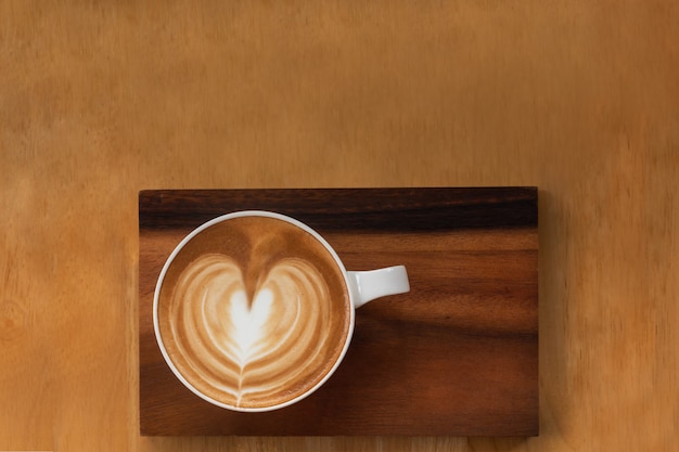 Top down view white cup of heart latte art coffee place on wooden table with copy space