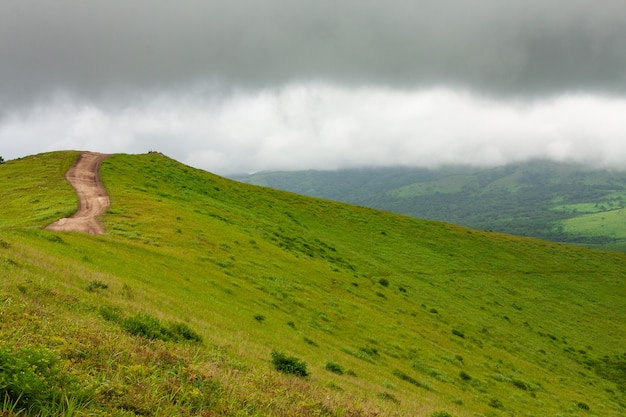 Top of a hill with a twisting dirt road, summer landscape in cloudy cloudy weather.