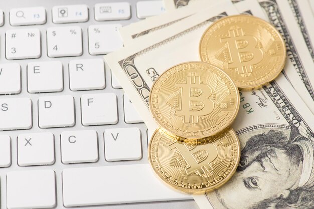 Photo top overhead above close up view photo of pile of golden bitcoin laying on american paper banknotes with white keyboard buttons on the background