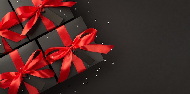 Top panoramic view photo of black gift boxes with red satin ribbon bow on isolated black background with copyspace