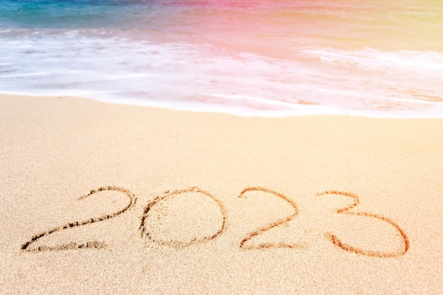 Top view of 2023 numbers written on the sand of coastline