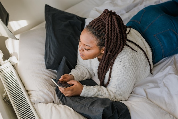 Top view African american female student dressed casually holding mobile phone and typing messages and communicating with friends via social networks using highInternet connection at home