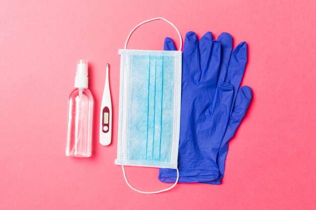 Top view of alcohol hand sanitizer, latex gloves, digital thermometer and medical mask on pink background. Virus protection equipment concept with copy space