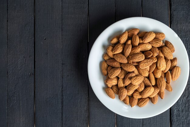 Photo top view of almonds on a white dish on black wooden table.