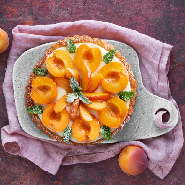 Top view of apricot tart with mint leaf on ceramic board on dark wall