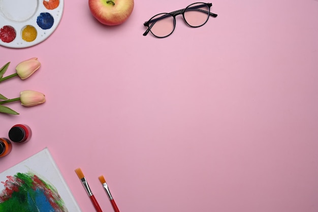 Photo top view artist workspace with color palettes paint brushes bouquet of pink tulips on pink pastel background