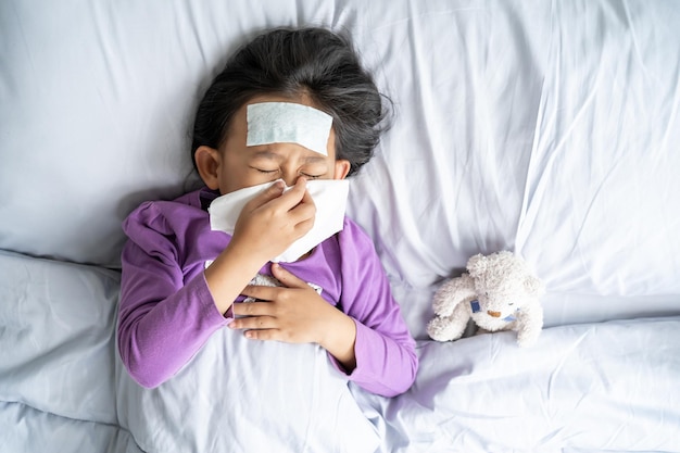 Top view Asian child girl sick with sneezing on the nose and cold cough on tissue paper because weak Sick child with fever and illness in bed