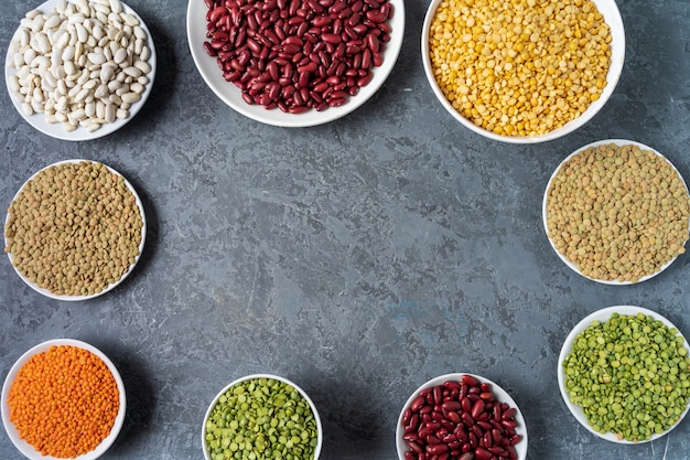 Top view of assortment of peas, lentils, beans and legumes over gray background.