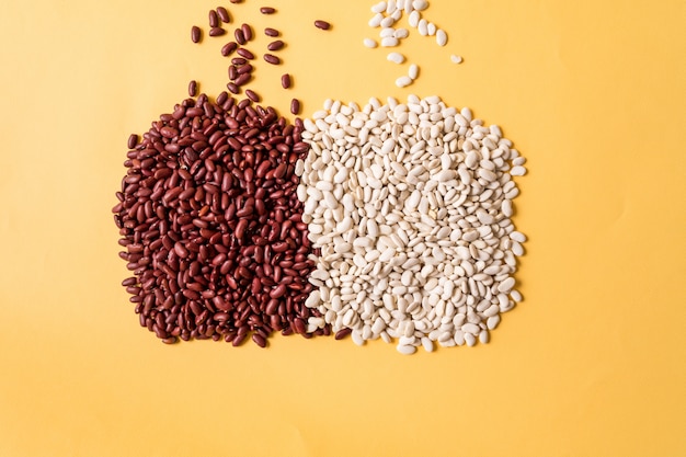 Top view of assortment of white and red beans over yellow background.