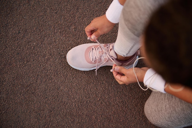 Top view of an athlete tying sneaker laces crouched on a treadmill while preparing for a run outdoor. Sport, active healthy lifestyle, health and body care concept with copy space