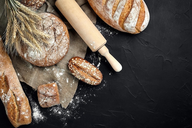 Top view of baguette baked bread flour and wheat spikes composition with wheat flour sprinkled around on a dark background