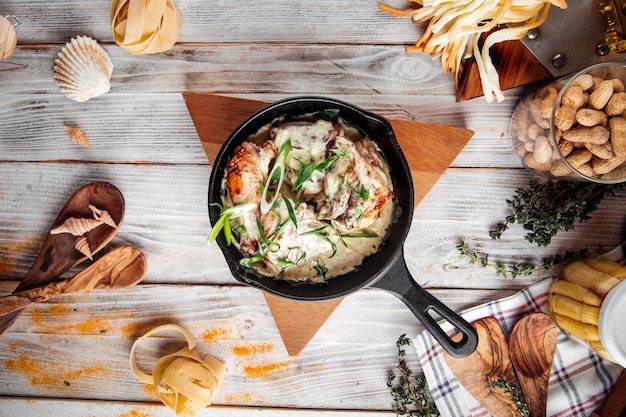 Top view on baked chicken in creamy sauce with green onions in cast iron pan