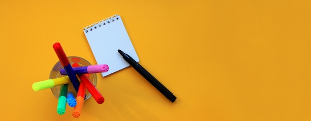 Top view banner of felt-tip pens and blank notepad on yellow 