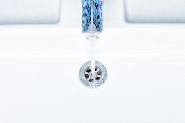 Photo top view of a bathroom sink tap with running away water as water economy concept