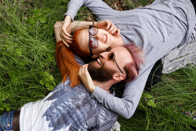 Top view of a beautiful couple, seated down on a grass, seated down with turned heads wear in sunglasses.