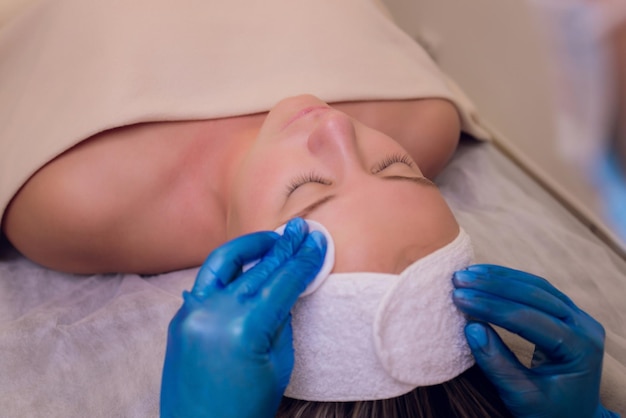 Top view of beautiful young woman getting face skin treatment Cosmetician is undertaking the procedure applying cream