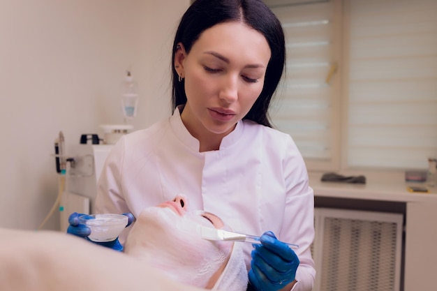 Top view of beautiful young woman getting face skin treatment Cosmetician is undertaking the procedure applying cream