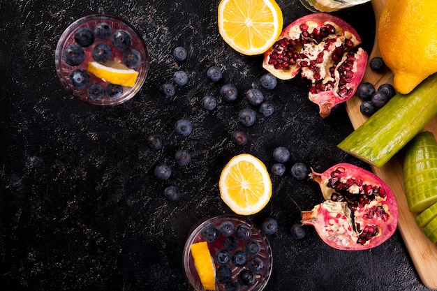 Top view of berries, pomegranate, cucumber and lemons on dark vintage wooden board