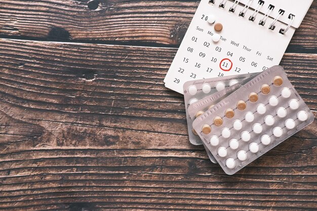 Top view of birth control pills and a calendar on wooden desk