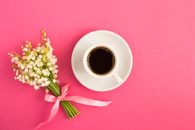 Top view of black coffee and bouquet of lilies of the valley on the pink