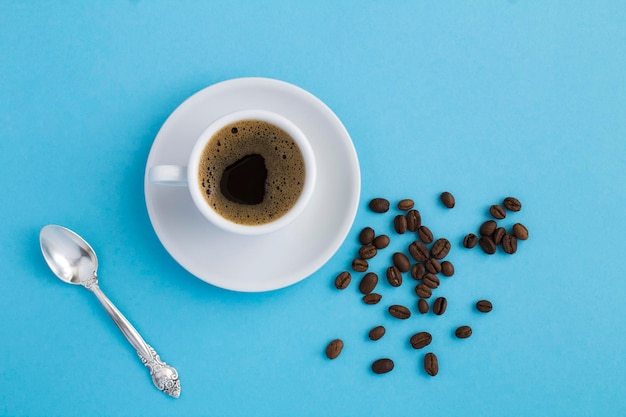 Top view of black coffee in the white cup and coffee beans on the blue background Closeup Copy space