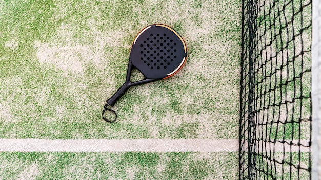 Top view of a black padel racket on a green court grass turf behind the net