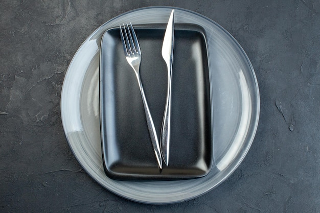 Top view black plate with fork knife and gray plate on dark surface