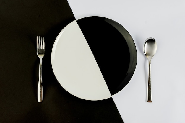 Top view of black and white colors of plate with silver spoon and fork on a black and white table