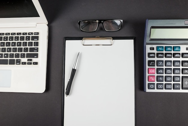 Top view of blank clipboard with laptop calculator and pen on black background copy space Place for text