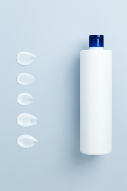 Top view blank label skincare white tube bottle with cosmetic sample swatch creamy texture product Blue background Copy space