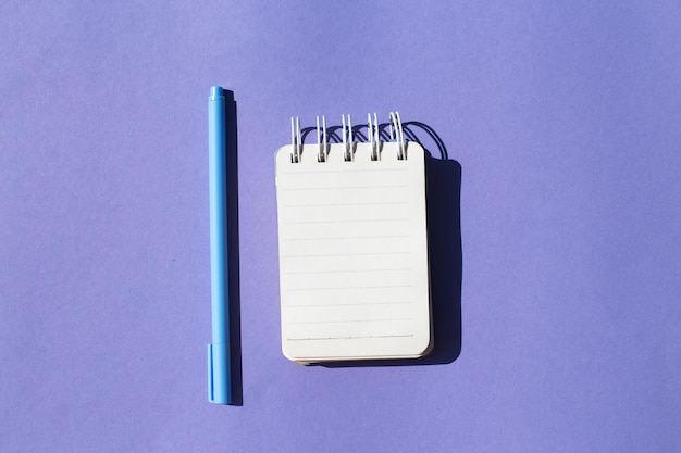 Top view of blank note paper with pen on purple background