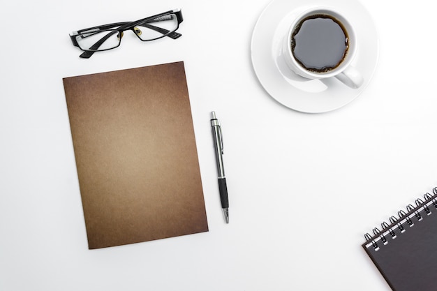 Top view blank notebook, pen and glasses on white desk background.