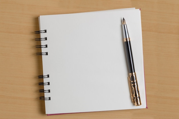 Top view of a blank notepad next to a pen on a wooden background.