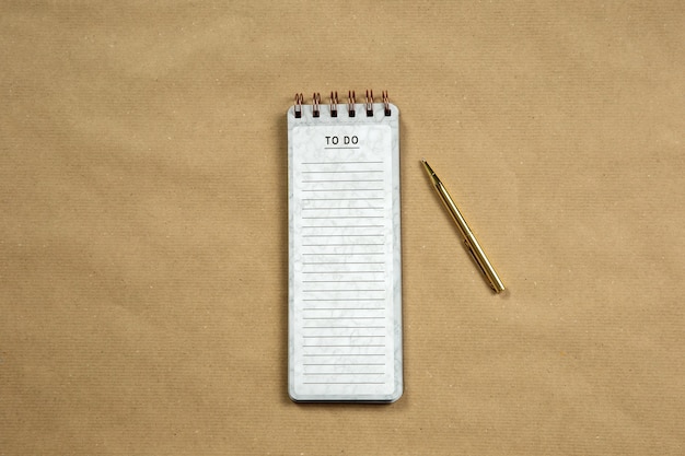 Top View of blank Notepad with empty To Do list on brown paper background, copy space or space for text, modern design with gold pen close-up