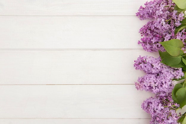 Top view of blooming lilac branches designed as one side frame on white wooden background Copy space