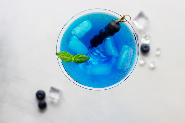 Top view of blue cocktail in martini glass with ice cubes mint and bluberries