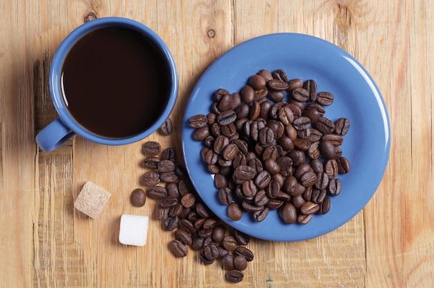 Top view on blue cup of coffee, saucers with beans and sugar cubes on old wooden background