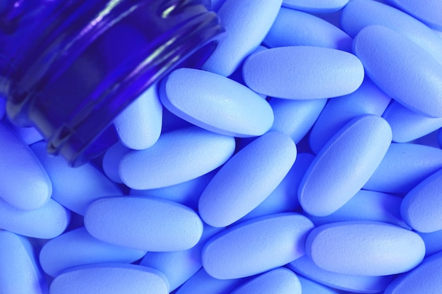 Top view of blue oval shaped pills scattered from vivid blue glass bottle