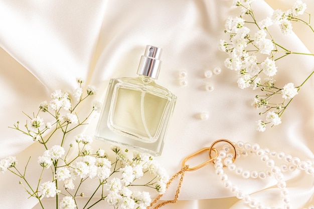 Top view of a bottle of women's perfume on a satin fabric pastel background with a pearl necklace and gypsophila advertising the fragrance