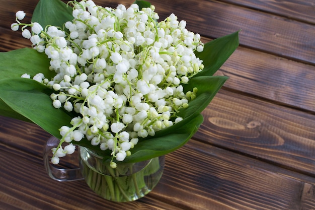 Top view of bouquet of lily of the valley in the glass jug on the wooden