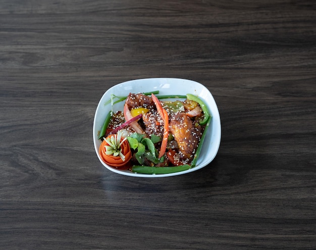 Top view of a bowl of deliciously roasted chicken with sesame seeds and vegetables on the table