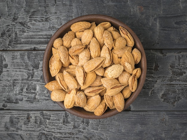 Top view of a bowl filled with unpeeled almonds on a black wooden table. Vegetarian food. Flat lay.