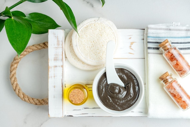 Top view of a bowl with handmade clay mask enriched with natural essential oil on wooden tray Spa procedures at home